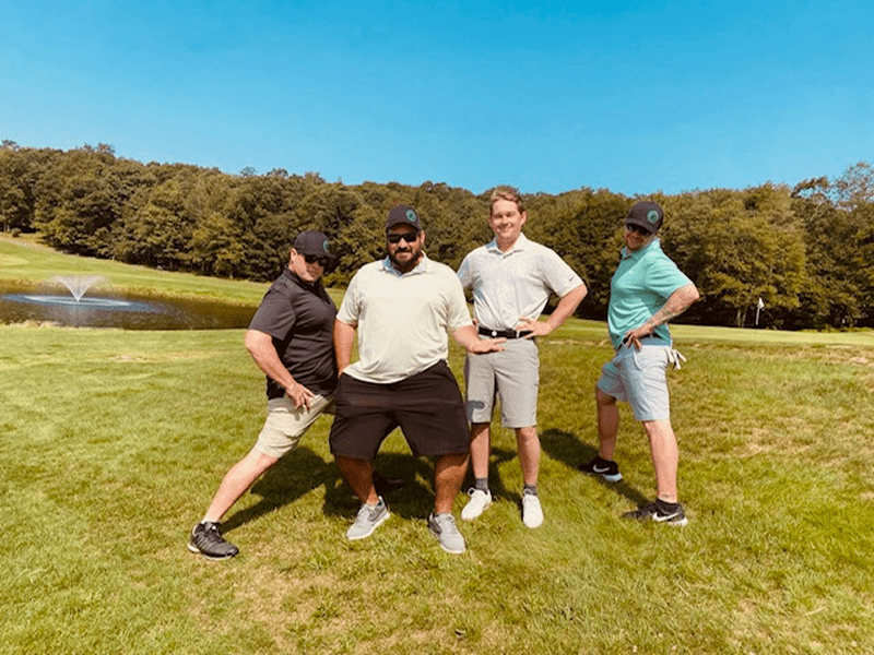 Four friends posing playfully on a sunny golf course.