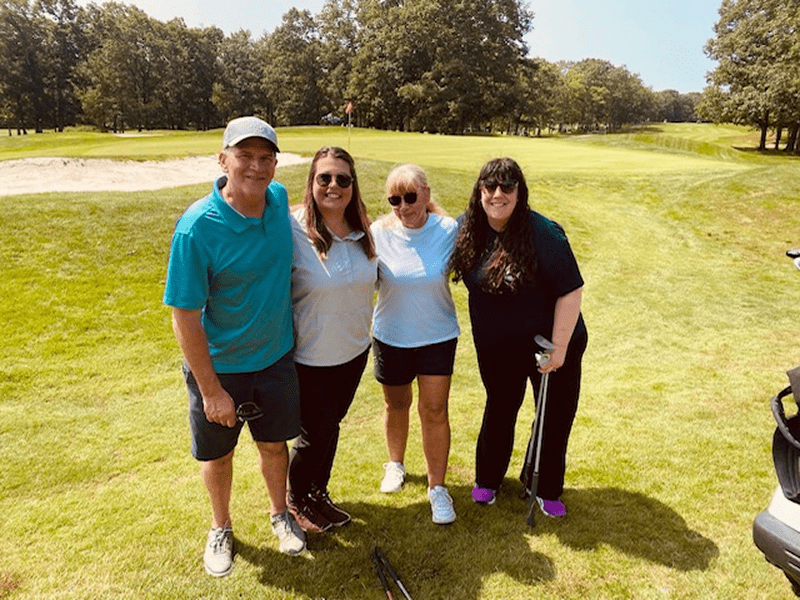 Four friends posing on a sunny golf course.
