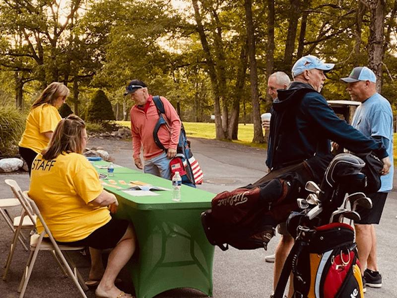 People gathered around a table outdoors on a sunny day.